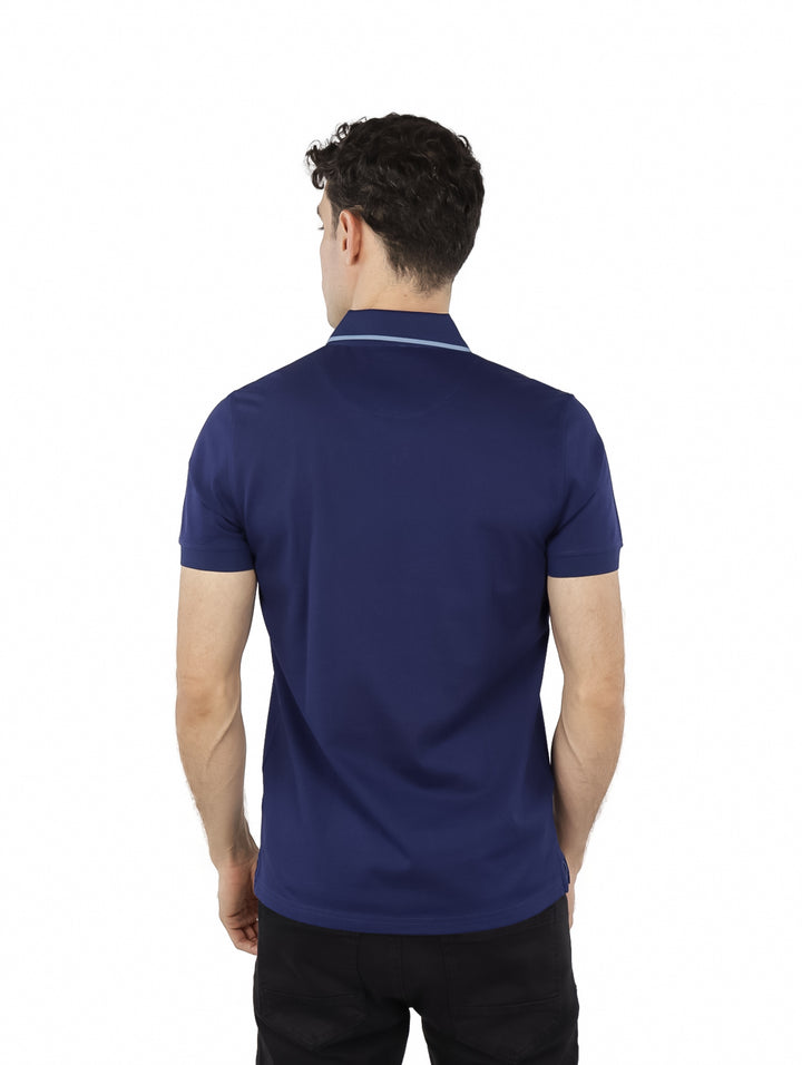 Hombre vistiendo una playera polo color azul medieval de manga corta con cuello y logo blanco pequeño en el pecho.