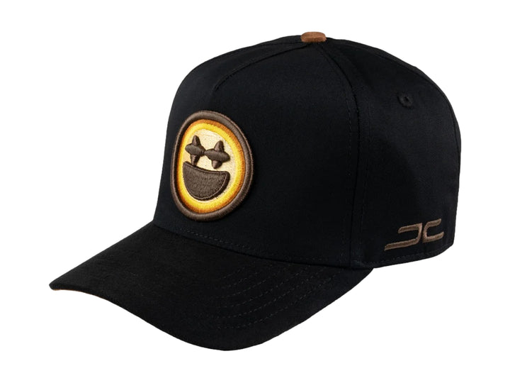 Gorra negra JC HATS con parche amarillo de carita feliz en el frente y detalle bordado lateral.