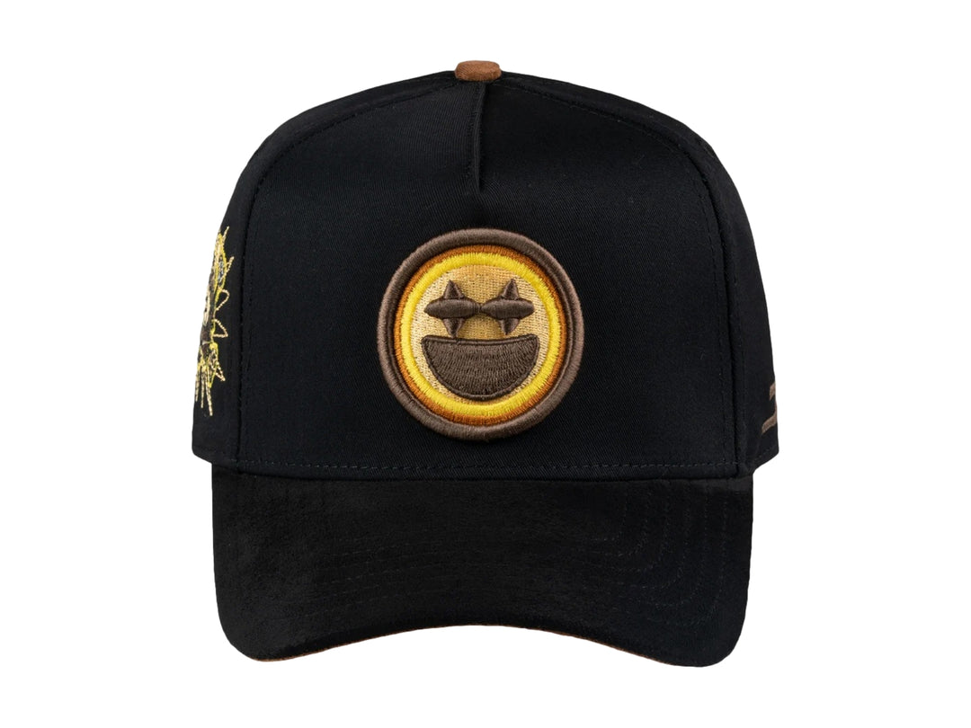 Gorra negra JC HATS con parche amarillo de carita feliz en el frente y detalle bordado lateral.