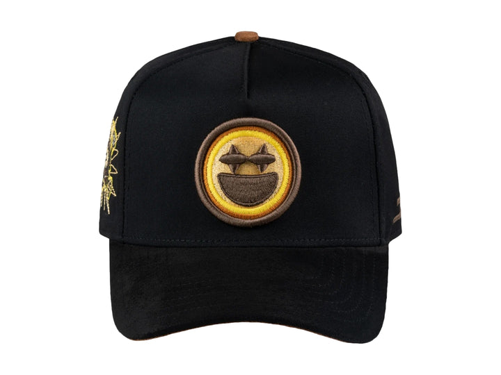 Gorra negra JC HATS con parche amarillo de carita feliz en el frente y detalle bordado lateral.