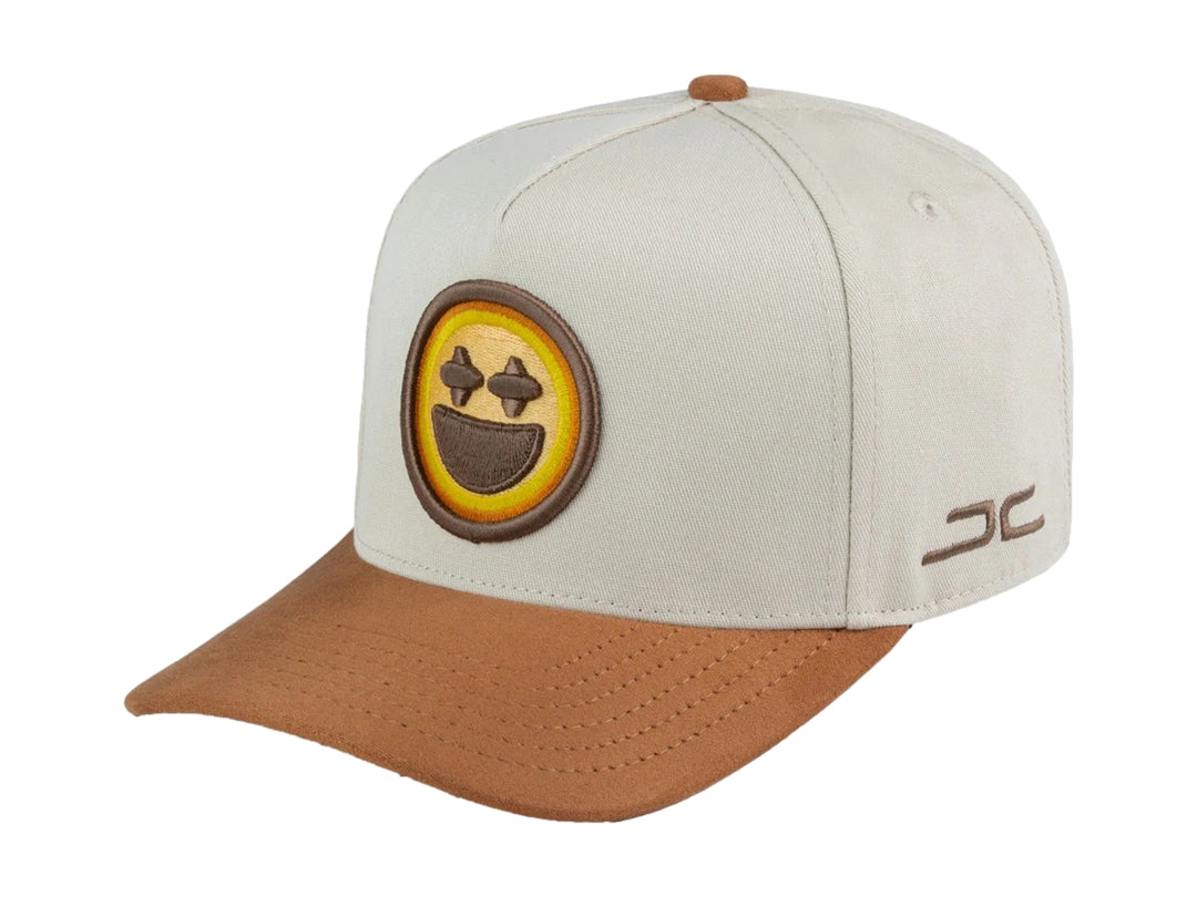Gorra snapback color beige con visera marrón y un parche frontal de carita feliz amarilla.