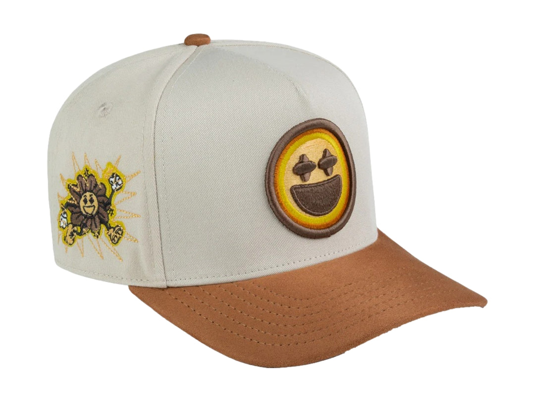 Gorra snapback color beige con visera marrón y un parche frontal de carita feliz amarilla.