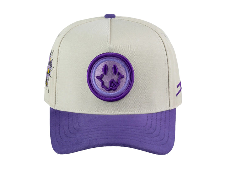 Gorra snapback color beige con visera y detalles en morado, incluye un parche circular frontal con diseño gráfico.