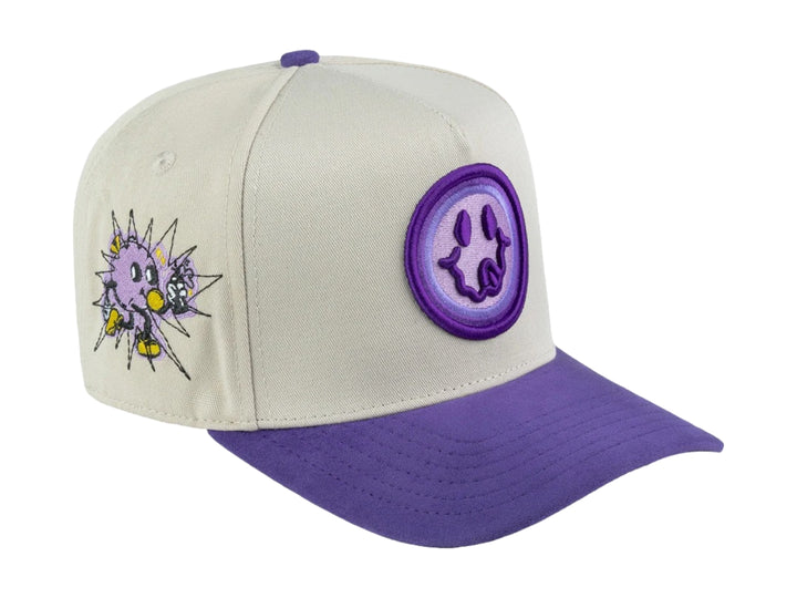 Gorra snapback color beige con visera y detalles en morado, incluye un parche circular frontal con diseño gráfico.