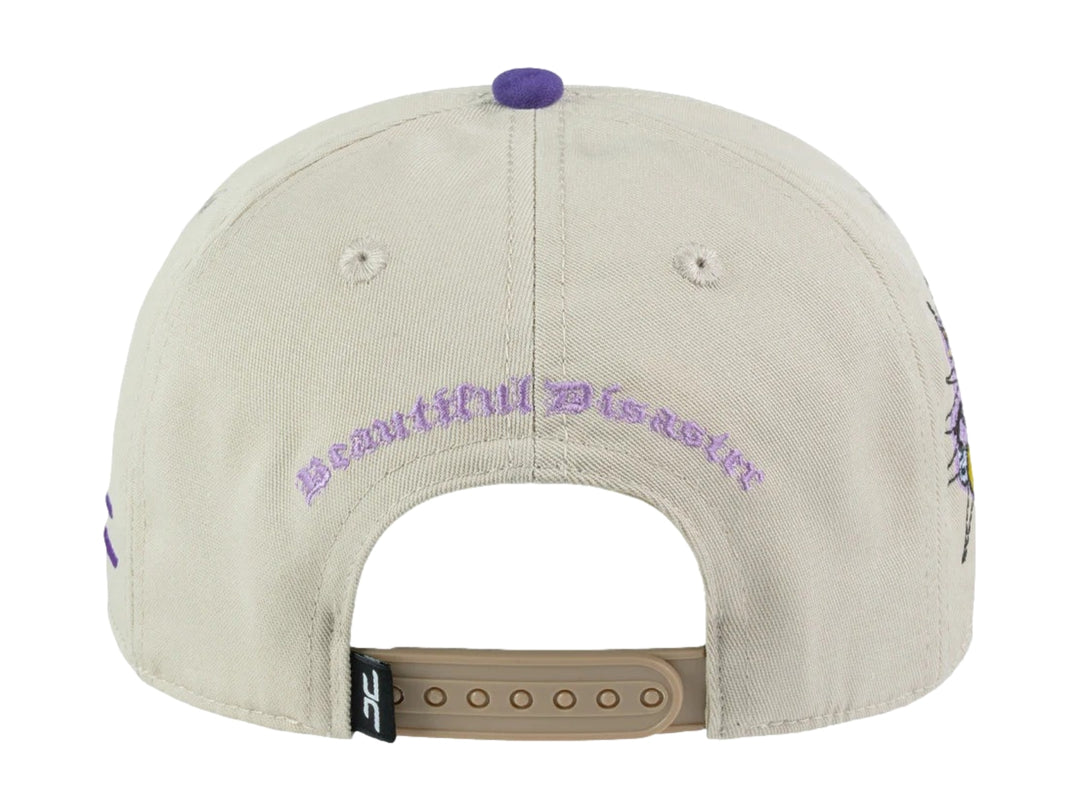 Gorra snapback color beige con visera y detalles en morado, incluye un parche circular frontal con diseño gráfico.