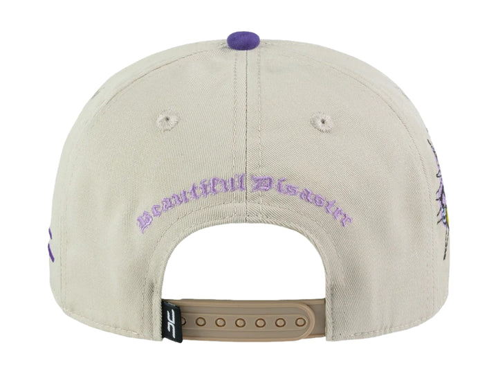 Gorra snapback color beige con visera y detalles en morado, incluye un parche circular frontal con diseño gráfico.