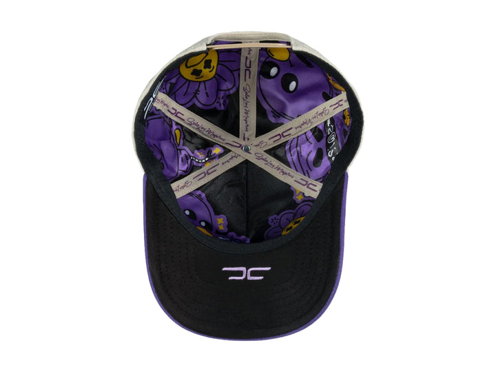 Gorra snapback color beige con visera y detalles en morado, incluye un parche circular frontal con diseño gráfico.