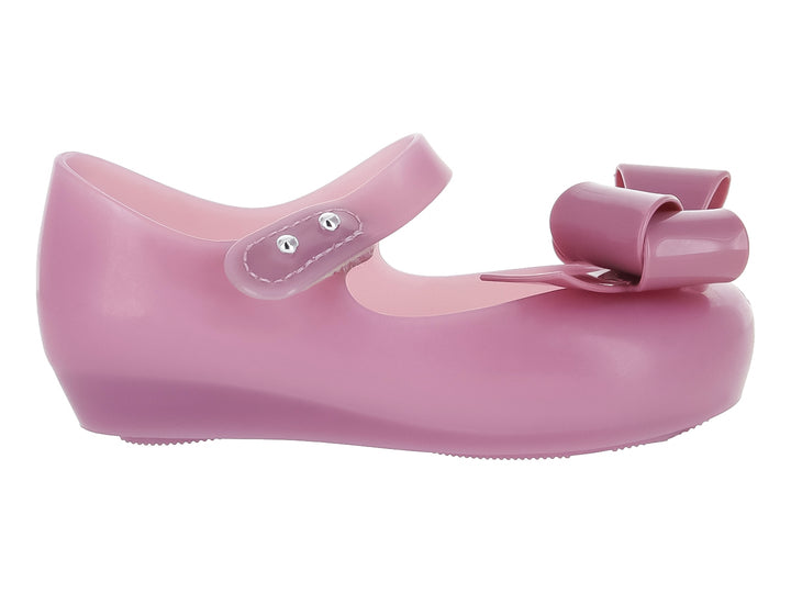 Zapato Mary Jane color lila para niña con moño frontal y correa con botones plateados.