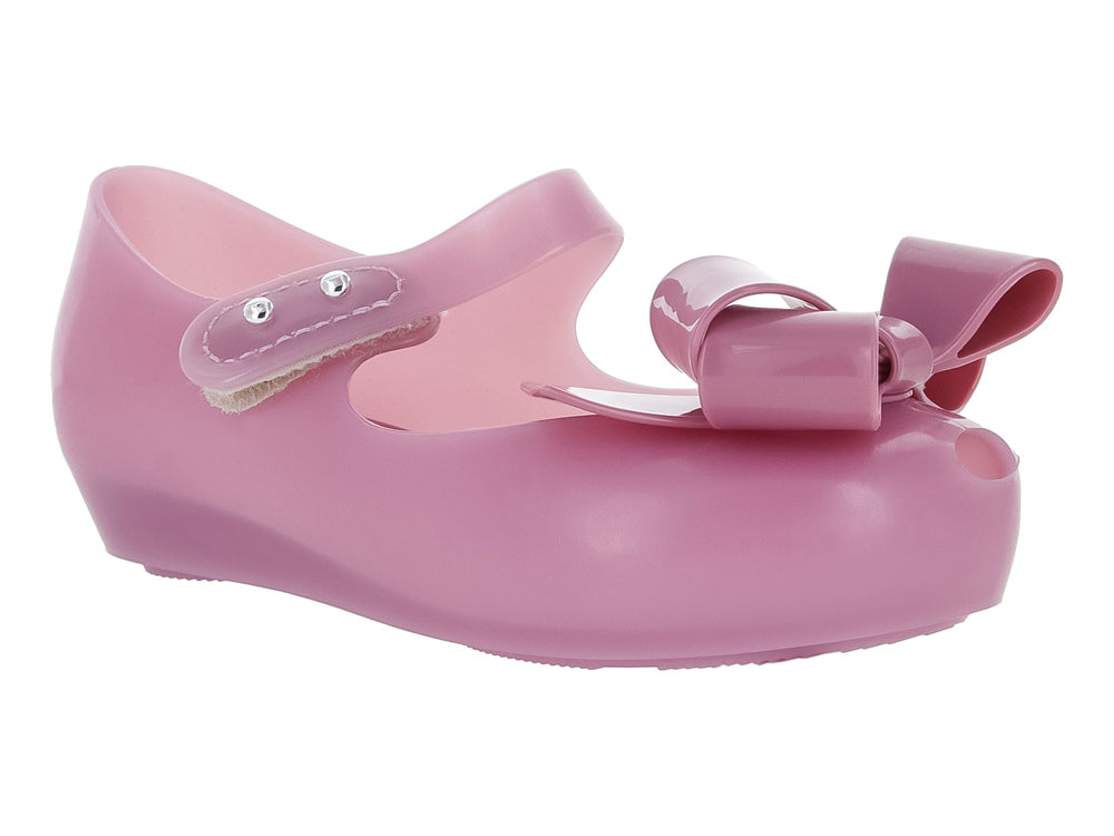Zapato Mary Jane color lila para niña con moño frontal y correa con botones plateados.