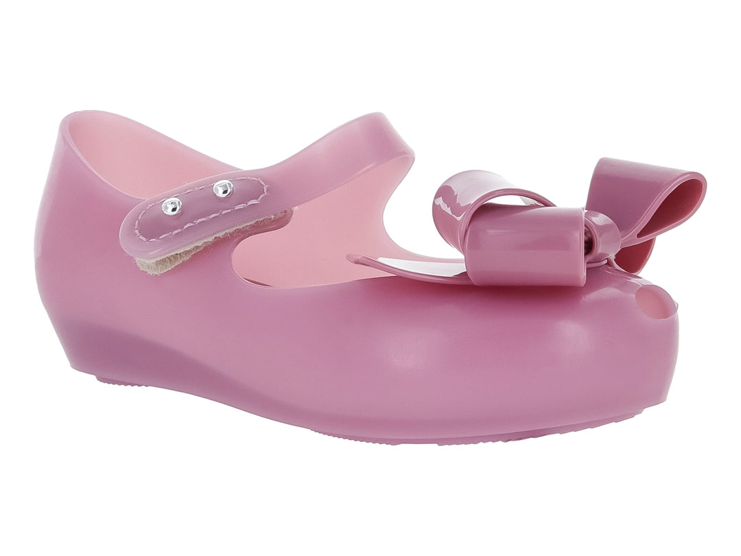 Zapato Mary Jane color lila para niña con moño frontal y correa con botones plateados.