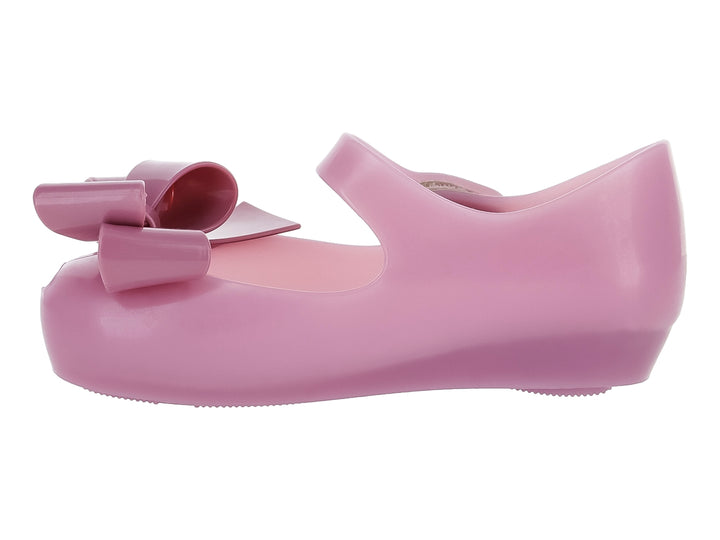 Zapato Mary Jane color lila para niña con moño frontal y correa con botones plateados.