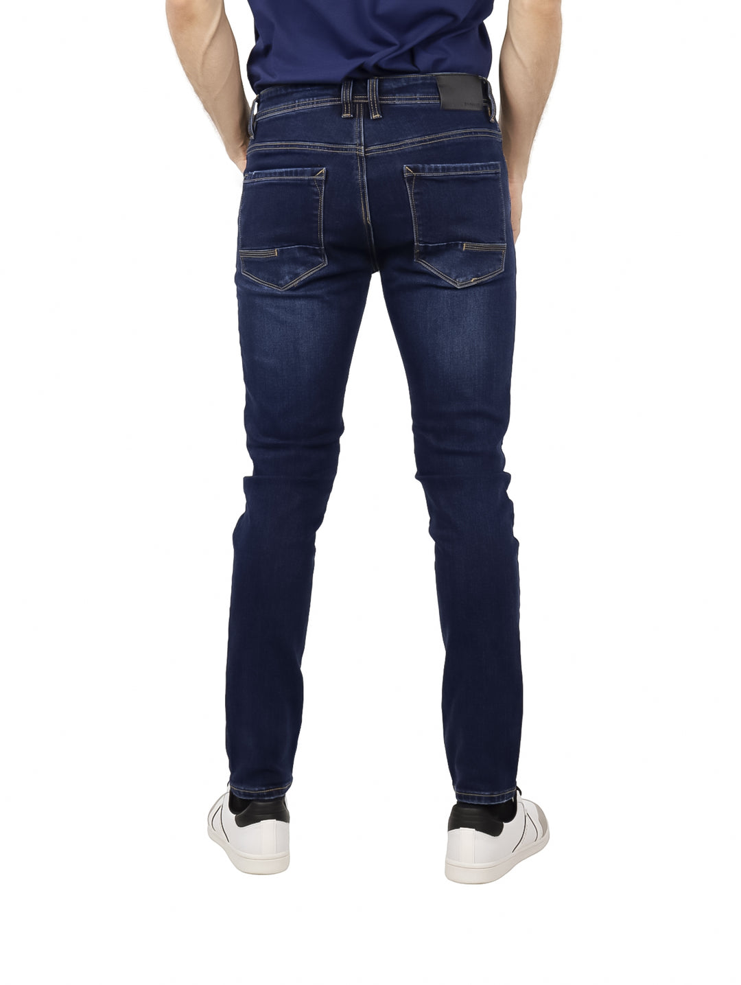 Hombre vistiendo pantalones jeans ajustados de color azul oscuro y tenis blancos.
