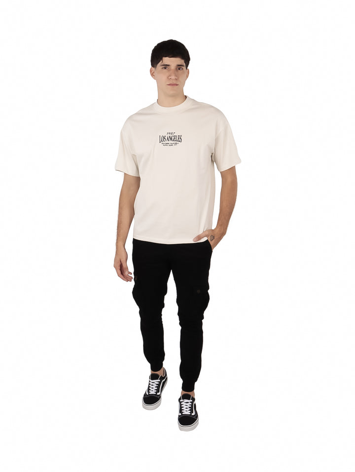 Hombre vistiendo playera oversize color beige con estampado de Los Angeles en el pecho.