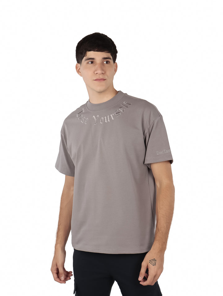 Hombre vistiendo una playera oversize de color gris con detalles de texto en el pecho y manga.