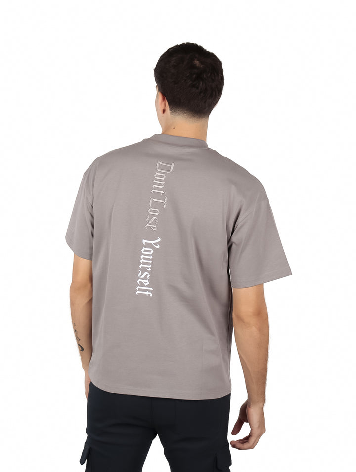 Hombre vistiendo una playera oversize de color gris con detalles de texto en el pecho y manga.