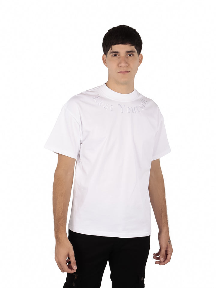 Hombre vistiendo una playera blanca de manga corta con texto en relieve en el pecho.
