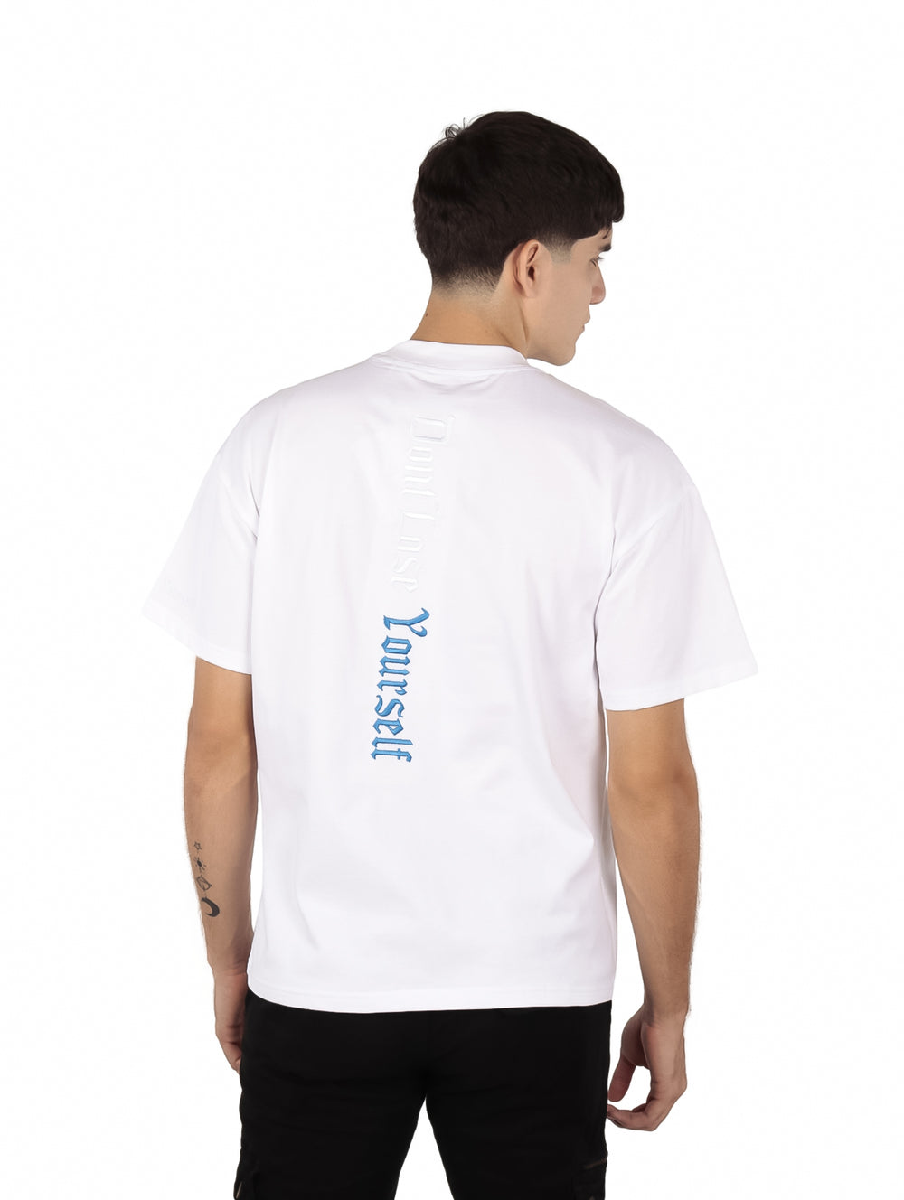 Hombre vistiendo una playera blanca de manga corta con texto en relieve en el pecho.