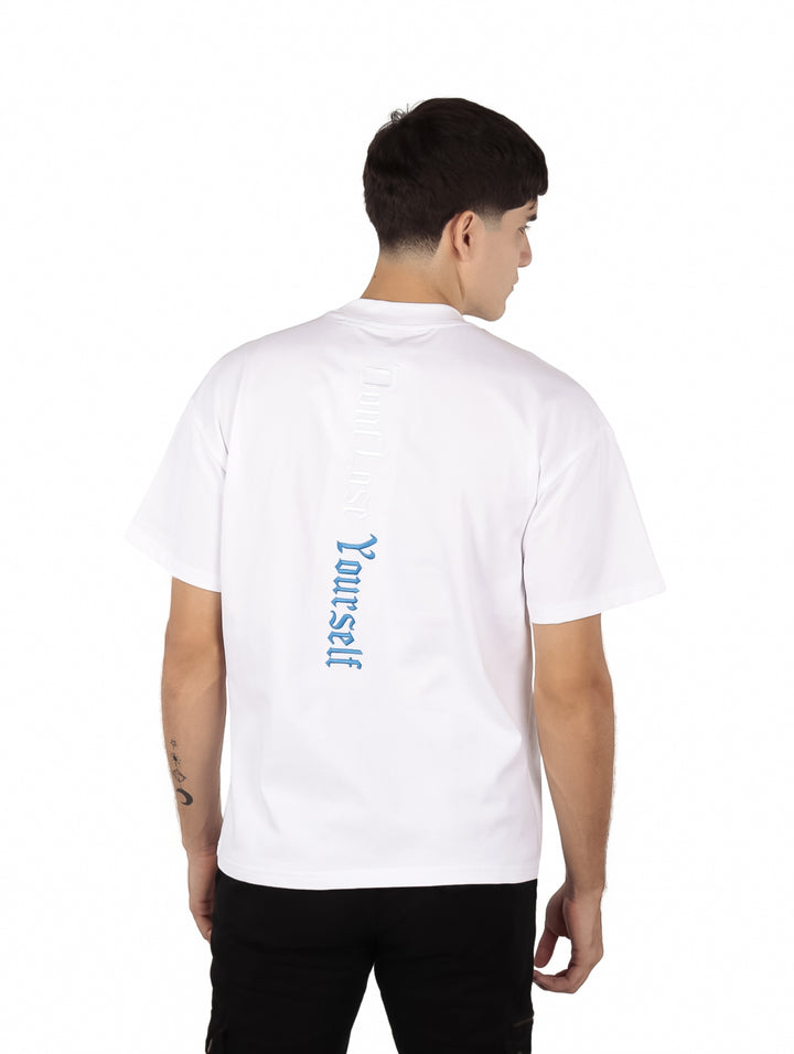 Hombre vistiendo una playera blanca de manga corta con texto en relieve en el pecho.