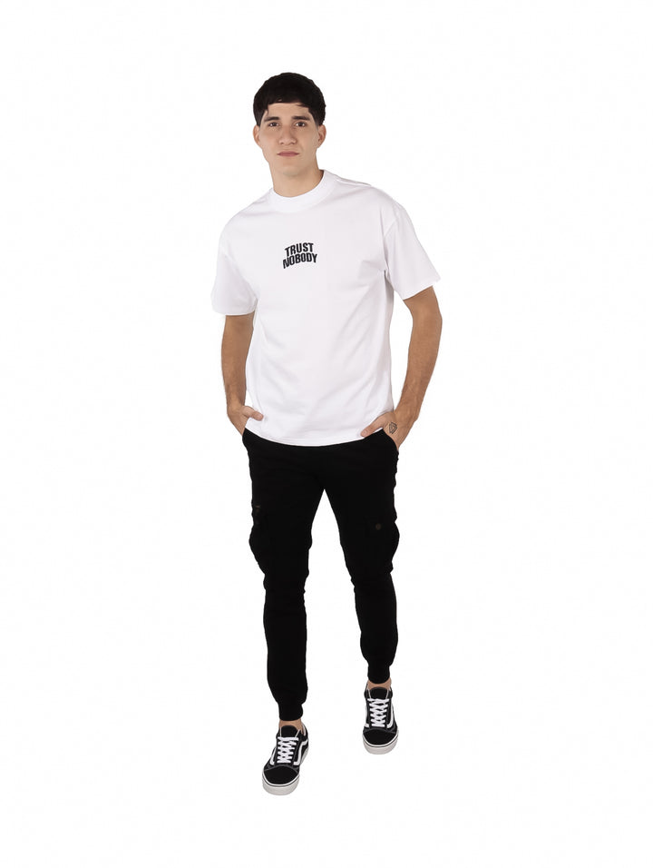 Hombre vistiendo una playera blanca oversize de manga corta con texto negro en el pecho.