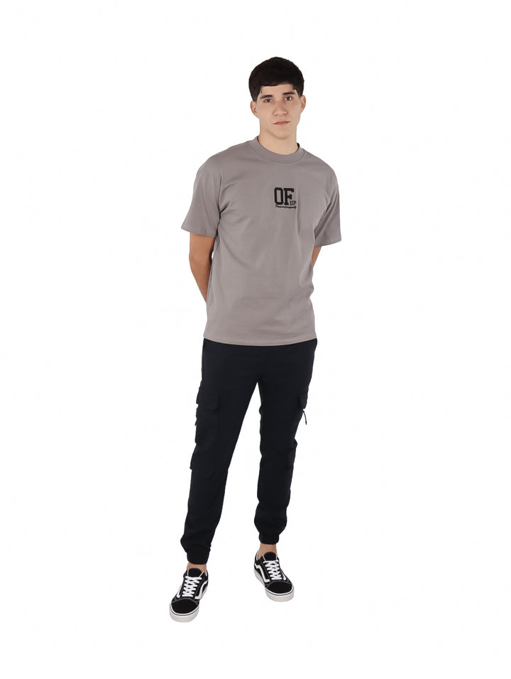 Hombre vistiendo una playera de manga corta color gris con un logotipo negro en el pecho.