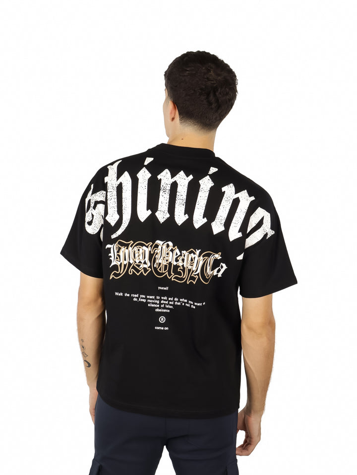 Hombre vistiendo playera negra de manga corta con estampado blanco en el pecho.