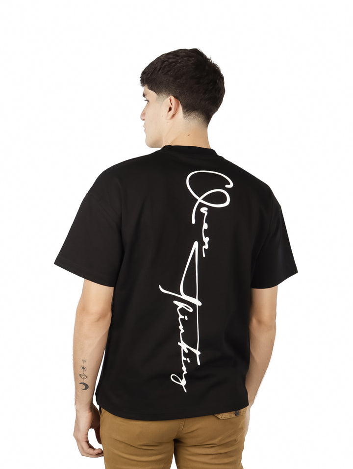 Hombre vistiendo playera negra de manga corta con detalle de texto blanco en el área del cuello.