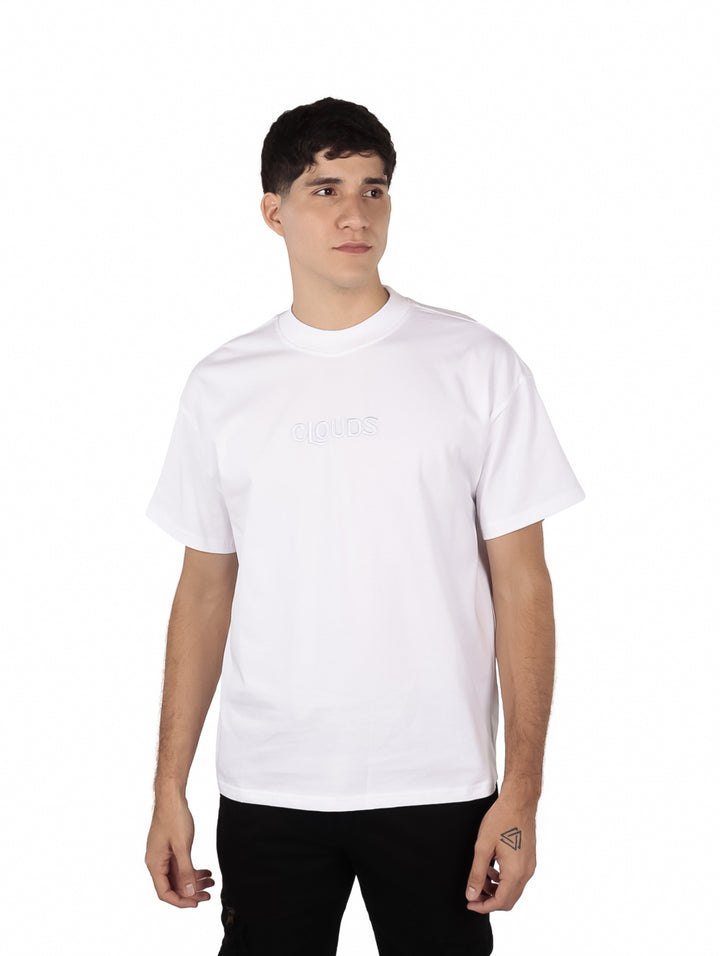 Hombre vistiendo una playera blanca de manga corta con texto en relieve en el pecho.