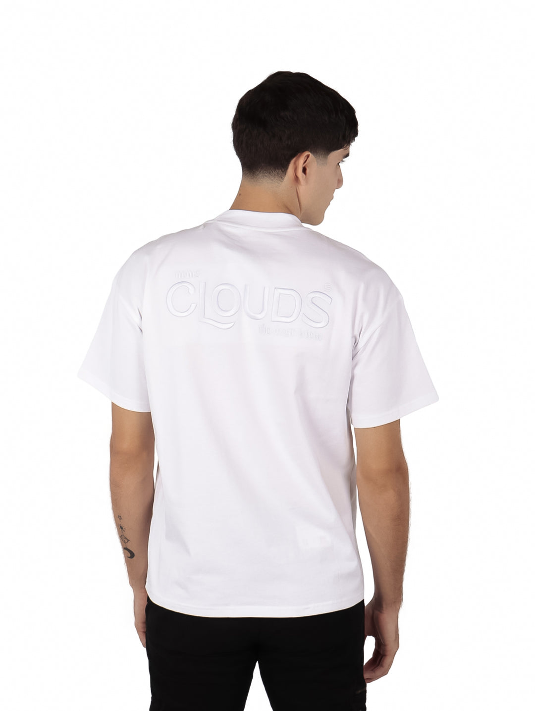 Hombre vistiendo una playera blanca de manga corta con texto en relieve en el pecho.