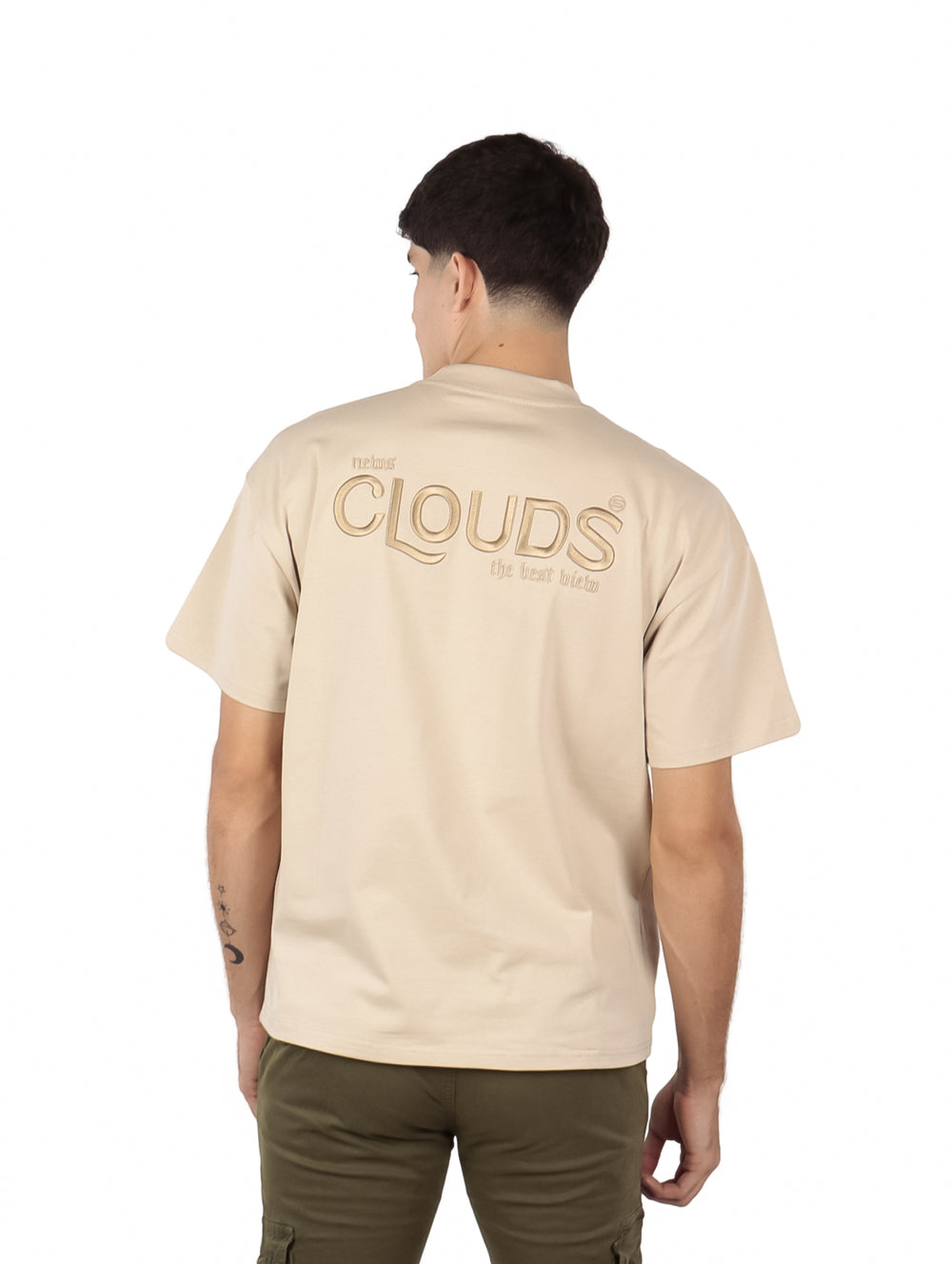 Hombre vistiendo playera oversize color beige con texto 'CLOUDS' en el pecho.