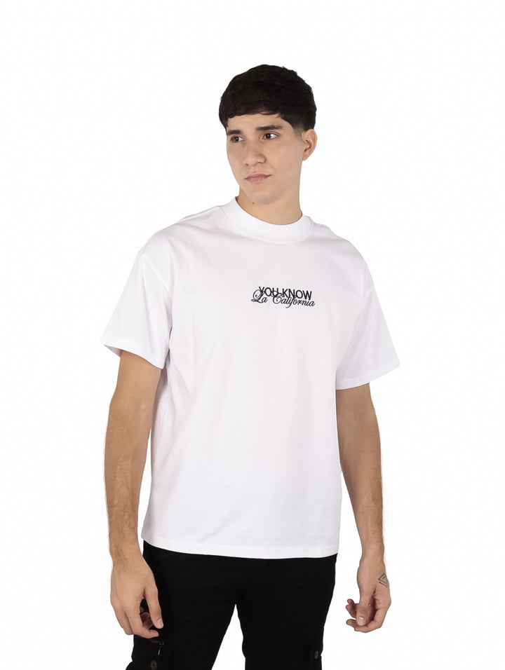 Hombre vistiendo una playera blanca oversize de manga corta con un pequeño estampado negro en el pecho.