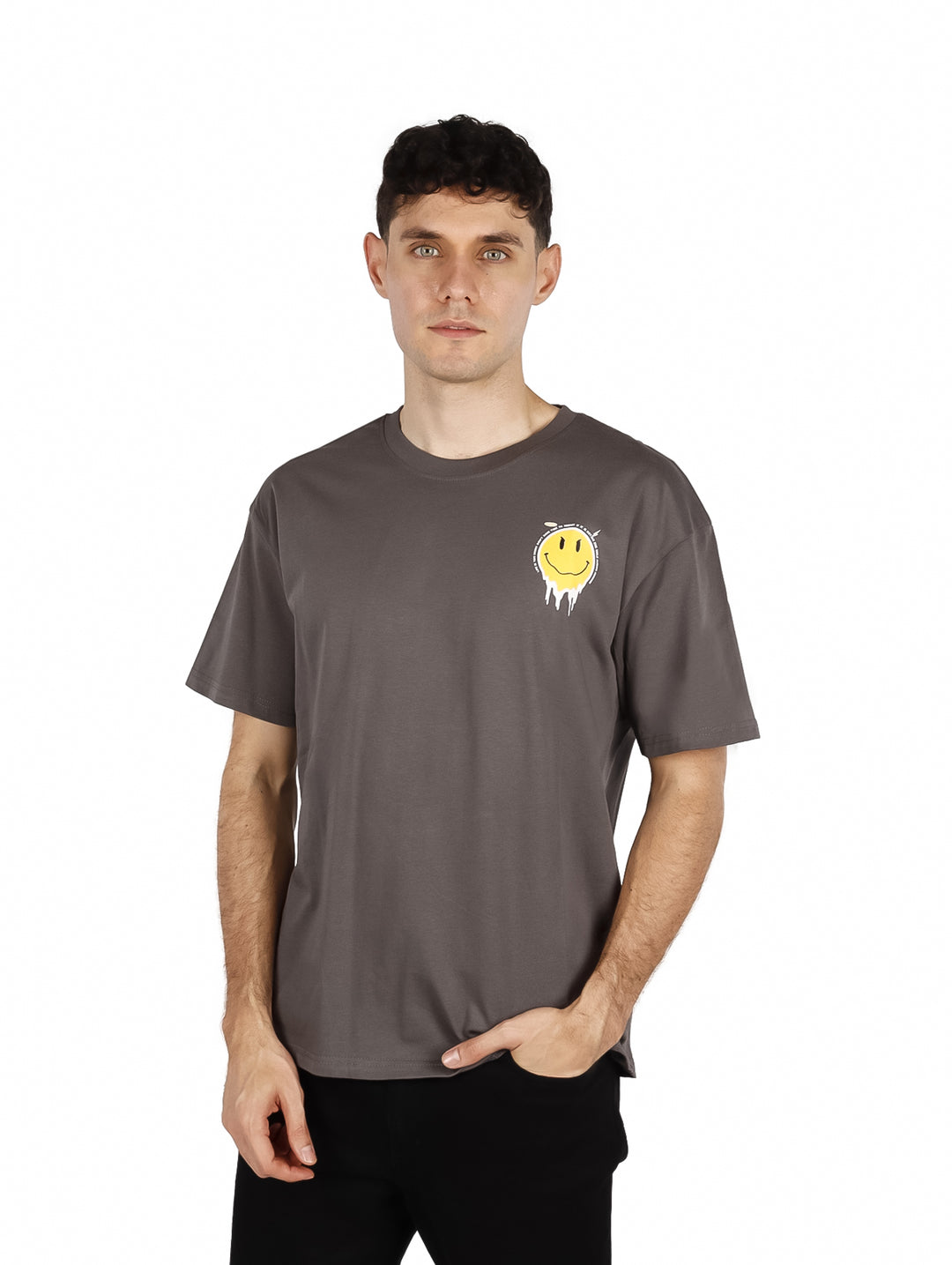 Hombre vistiendo playera oversize color gris con un pequeño gráfico de cara sonriente amarilla en el pecho.