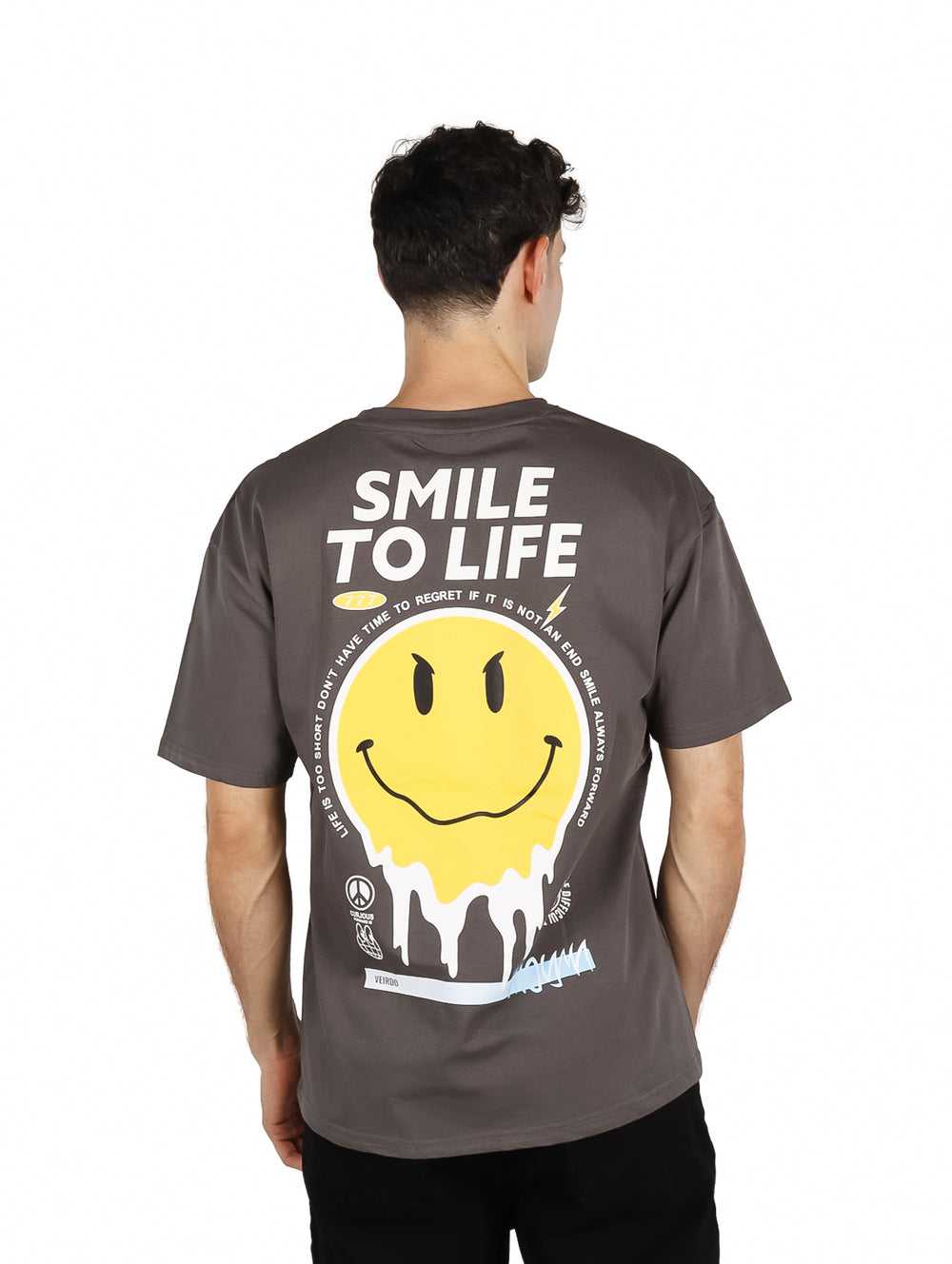 Hombre vistiendo playera oversize color gris con un pequeño gráfico de cara sonriente amarilla en el pecho.