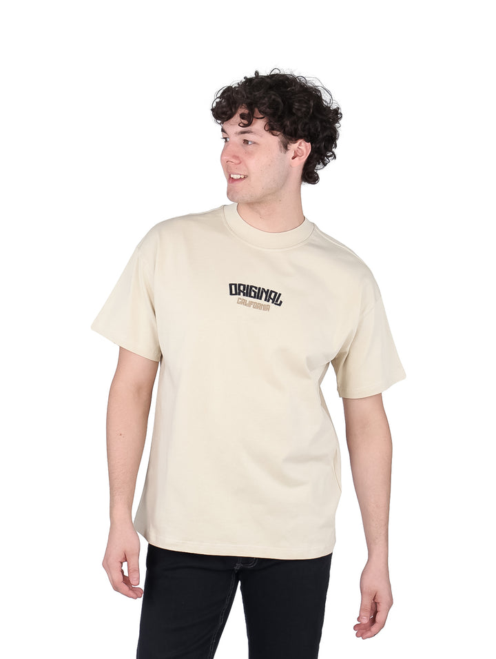 Hombre vistiendo playera oversize color beige con estampado negro en el pecho.