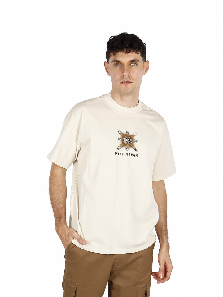 Hombre vistiendo playera oversize color beige con un diseño gráfico pequeño en el pecho.