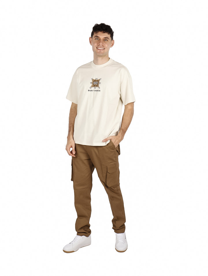 Hombre vistiendo playera oversize color beige con un diseño gráfico pequeño en el pecho.