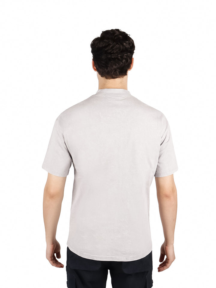 Hombre vistiendo playera oversize color gris con letras blancas en el pecho y cuello redondo.