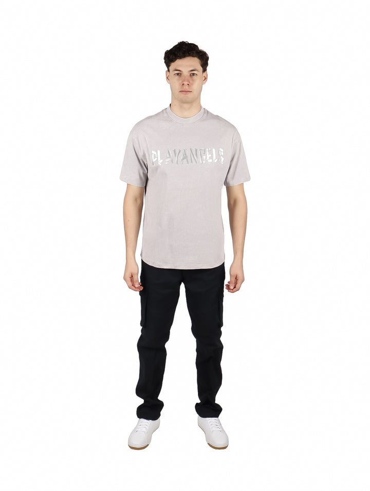 Hombre vistiendo playera oversize color gris con letras blancas en el pecho y cuello redondo.