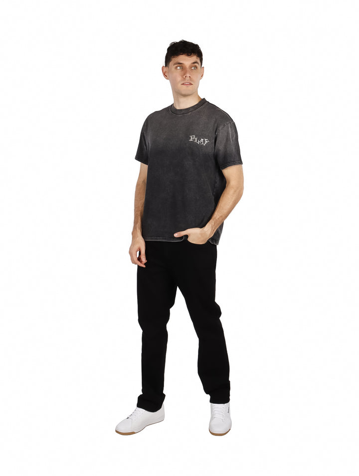 Hombre vistiendo playera oversize color negro con efecto lavado y texto &