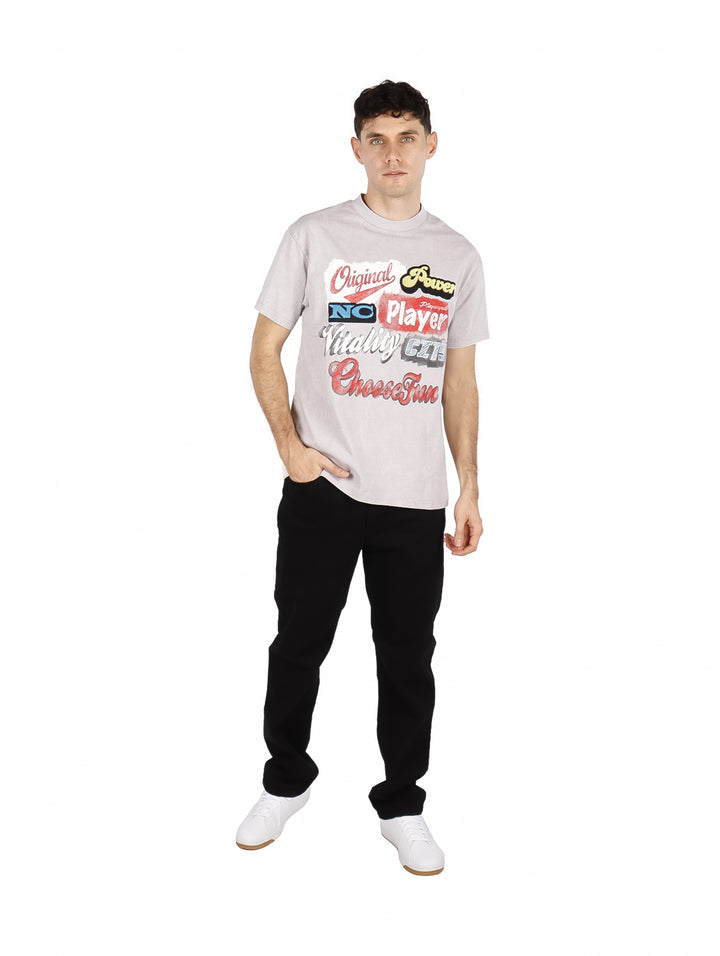 Hombre vistiendo playera oversize gris claro con estampado de letras multicolores en el pecho.