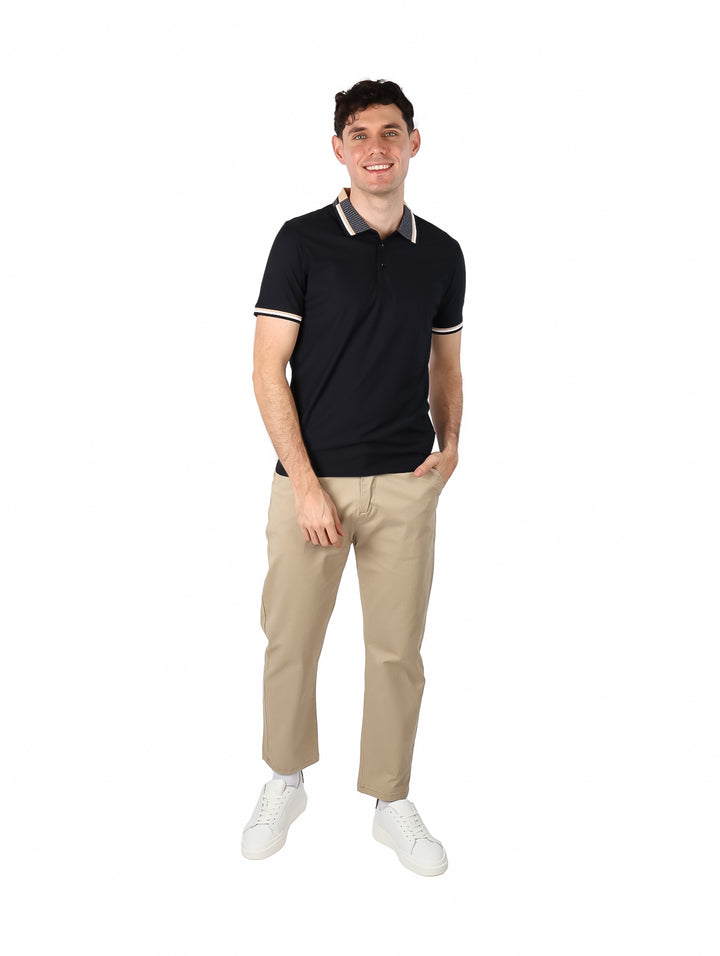 Hombre vistiendo playera polo color negro con cuello estampado y detalles beige en las mangas.