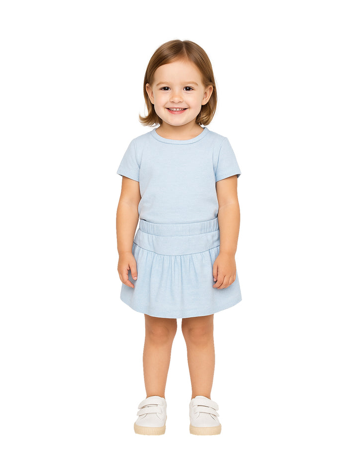 Niña pequeña vistiendo un conjunto de camiseta y falda en color azul claro con zapatos blancos.
