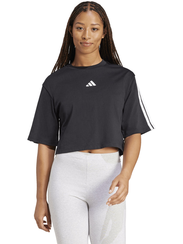 Mujer vistiendo playera holgada negra de algodón Adidas con rayas blancas en las mangas.