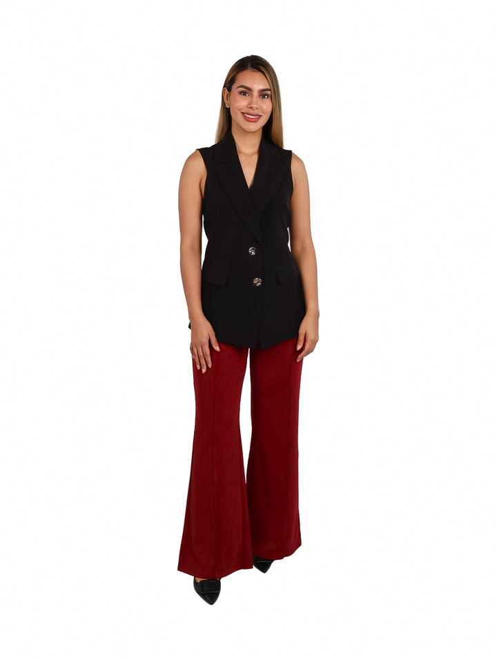 Mujer vistiendo un chaleco largo de color negro con botones dorados y pantalones rojos.