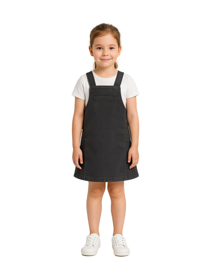 Niña vistiendo un overol de mezclilla color gris oscuro con una camiseta blanca y tenis blancos.
