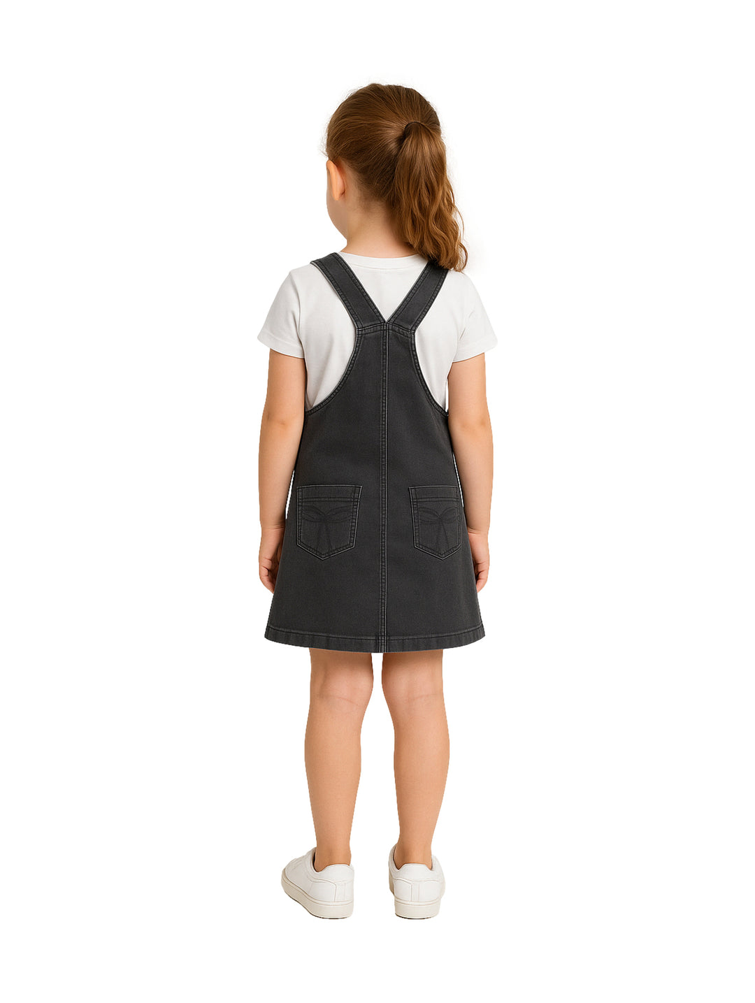 Niña vistiendo un overol de mezclilla color gris oscuro con una camiseta blanca y tenis blancos.