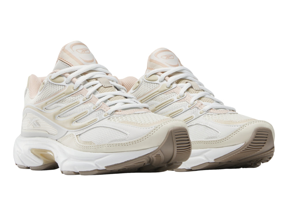 Tenis deportivo Reebok en color gris claro y blanco con detalles en beige y suela blanca.