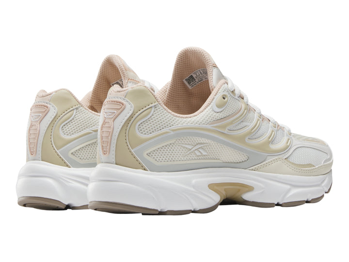 Tenis deportivo Reebok en color gris claro y blanco con detalles en beige y suela blanca.