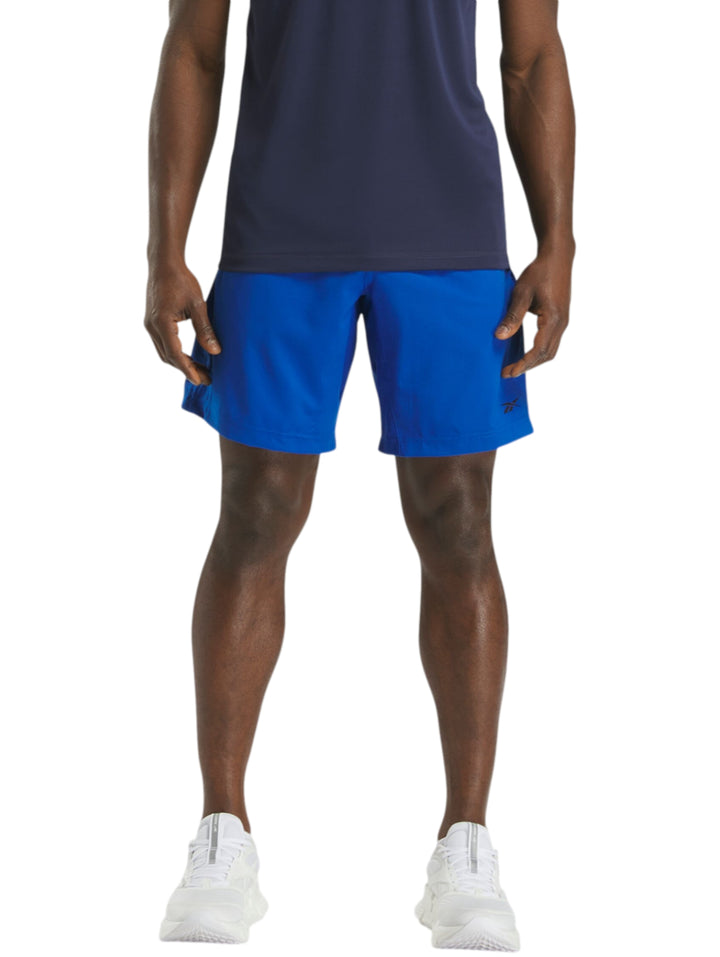 Hombre vistiendo shorts deportivos color azul marca Reebok con camiseta azul marino y tenis blancos.