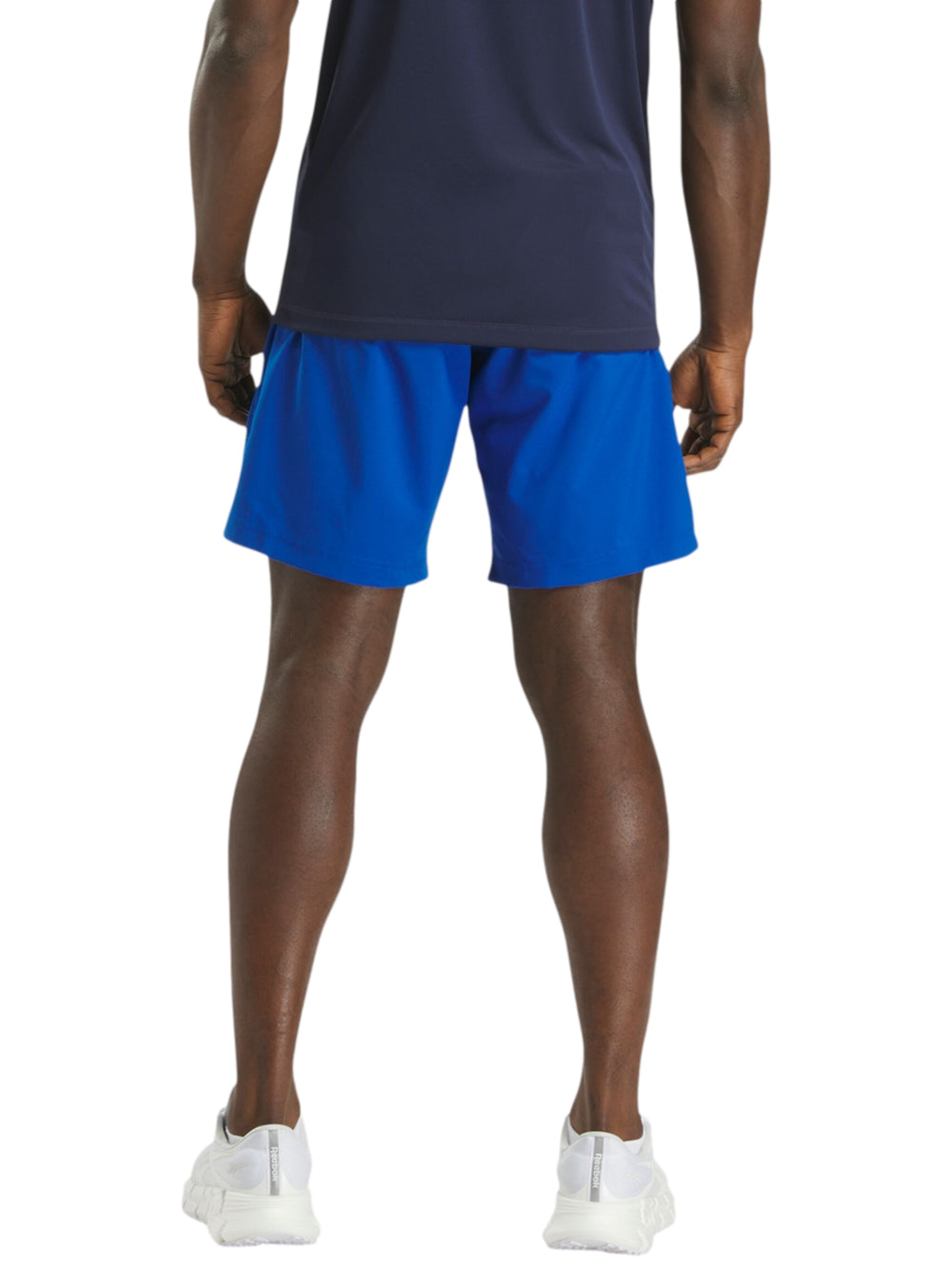 Hombre vistiendo shorts deportivos color azul marca Reebok con camiseta azul marino y tenis blancos.