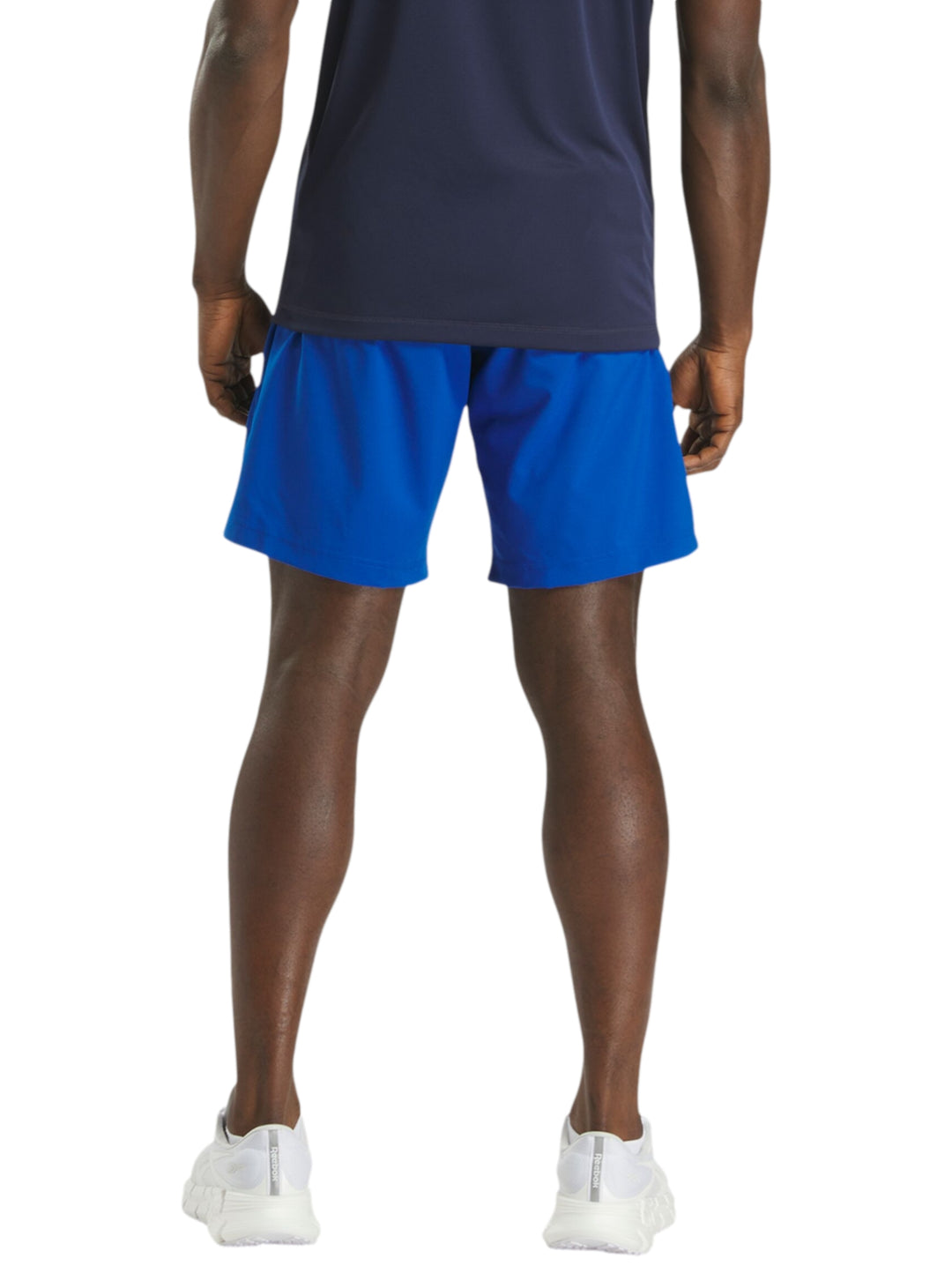 Hombre vistiendo shorts deportivos color azul marca Reebok con camiseta azul marino y tenis blancos.